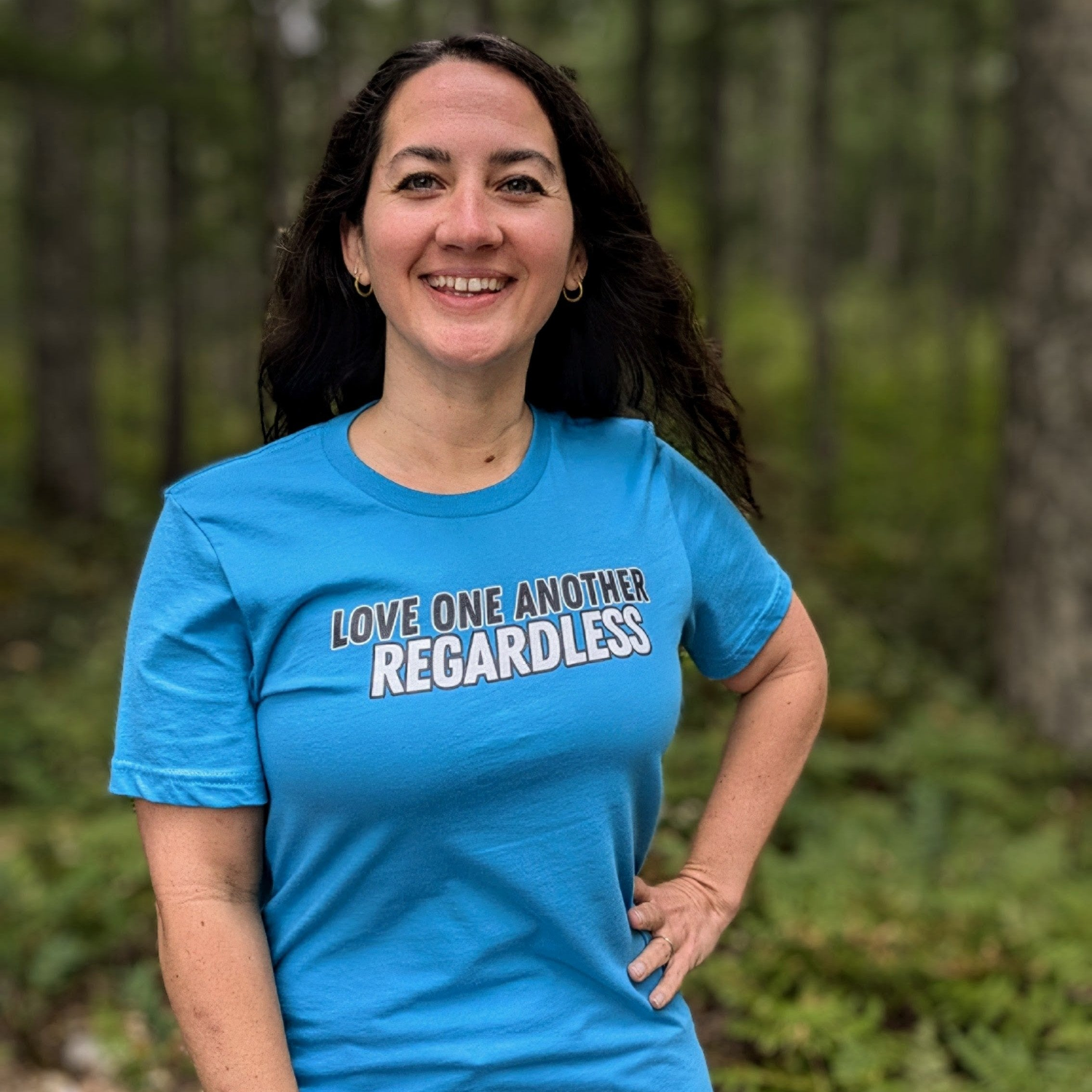 Woman wearing blue shirt printed with Love One Another regardless text in black and white