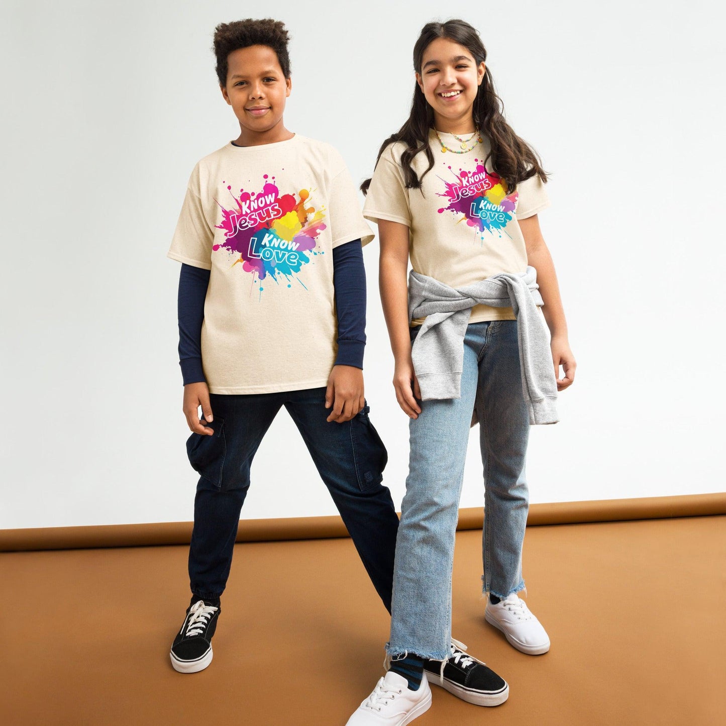 Boy and girl wearing Know Jesus Youth T-Shirts with white text on colorful paint splash graphic print